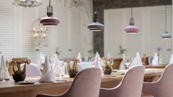 A dining area with a long table set for a meal, featuring chairs, plates, glasses, and potted plants.