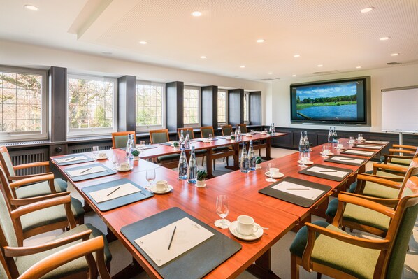 A conference room with long tables, chairs, and a large screen.