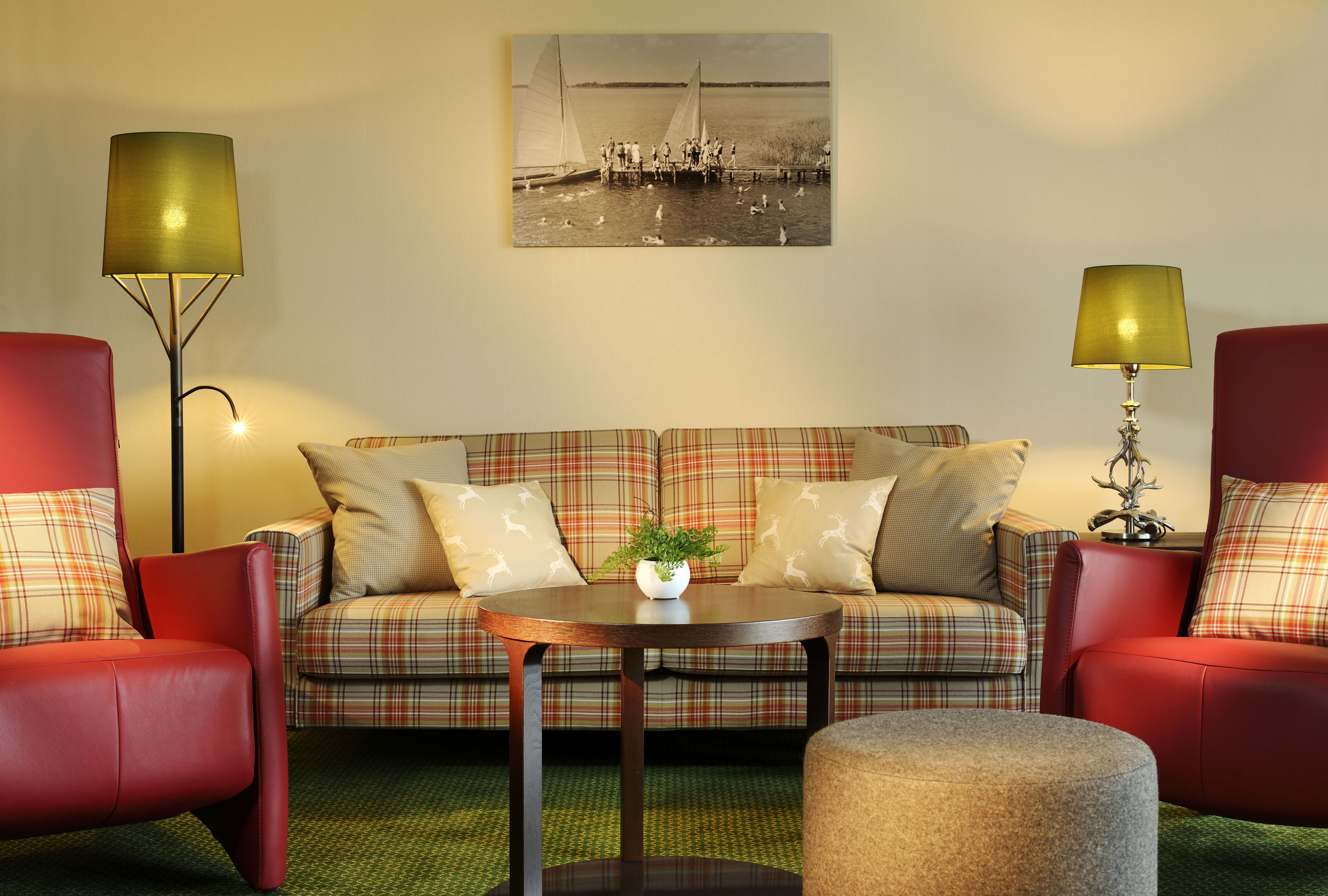 A living room with a plaid sofa, two red armchairs, a round coffee table, and a lamp.