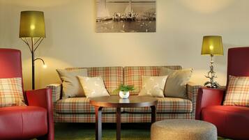 A living room with a plaid sofa, two red armchairs, a round coffee table, and a lamp.