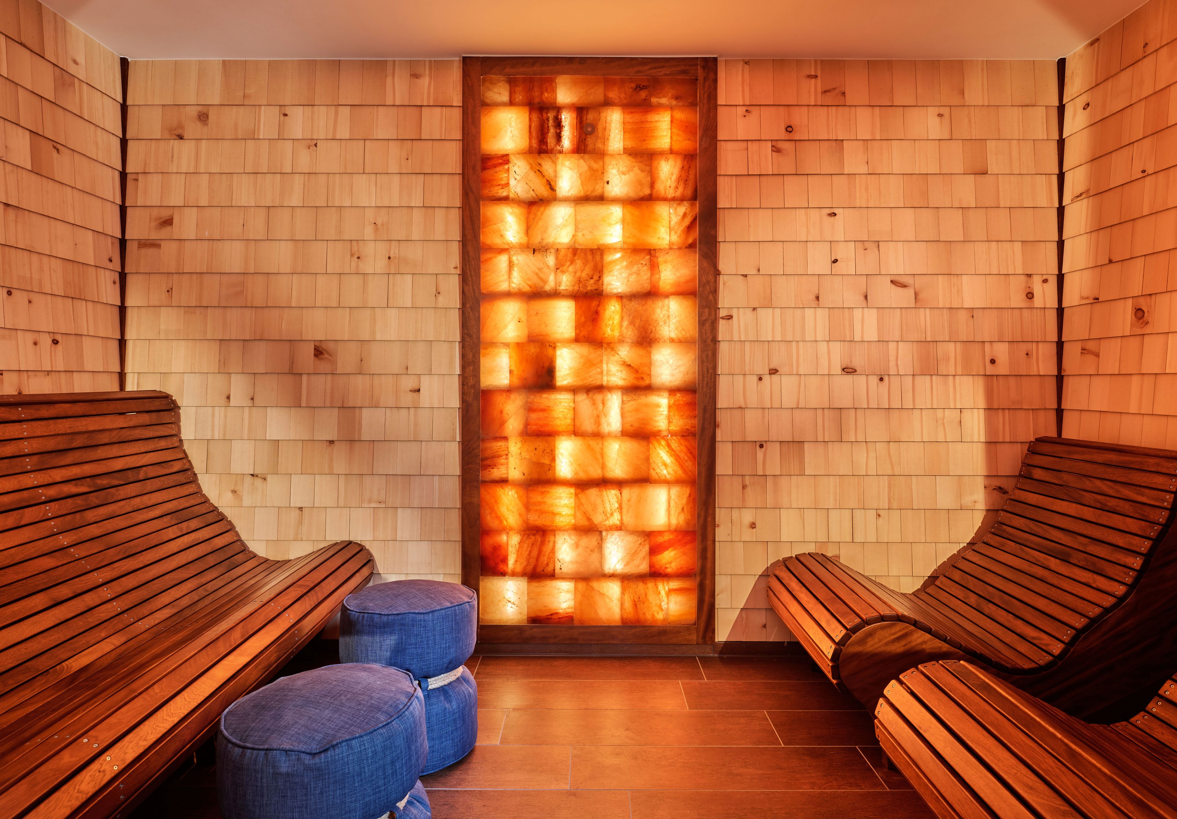 Een sauna met houten banken, een houten wand met een warmtepaneel en een betegelde vloer.