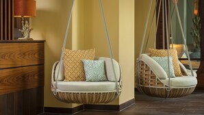 Dos sillones colgantes de mimbre con cojines estampados frente a una pared con rayas verticales.