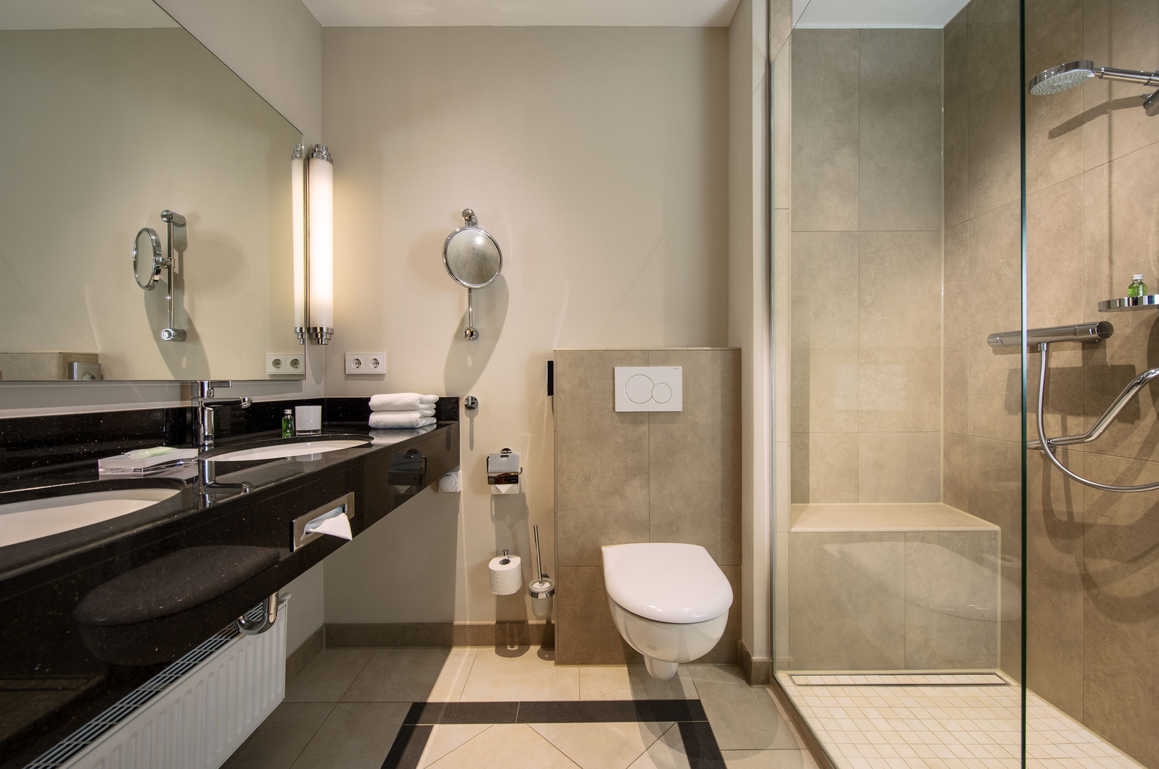 A modern bathroom with a black countertop, two sinks, a toilet, a shower, and a glass-enclosed shower area.