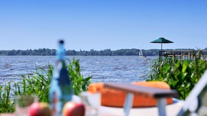 Vista a un lago con un muelle de madera, un velero y una mesa con manzanas y una botella.