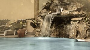A pool with a waterfall feature, surrounded by a rock wall and potted plants.