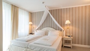 A double bed with a canopy, bedside tables with lamps, and a striped wallpaper background.
