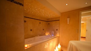 A modern bathroom with a large bathtub, a mirror, and candles on the floor.