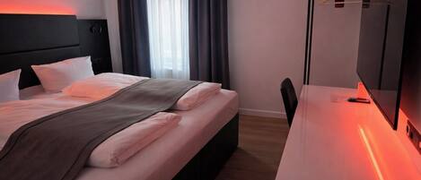 A hotel room with a bed, a desk, a chair, a TV, and a window with curtains.