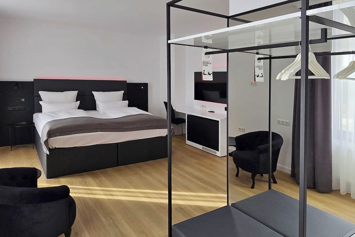 A modern hotel room with a bed, a desk, a chair, and a wardrobe.