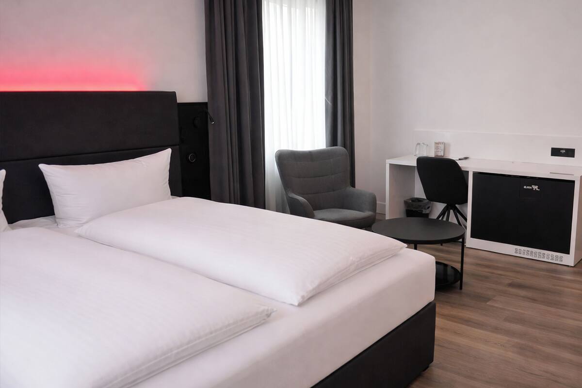 A hotel room with a large bed, a desk, a chair, and a small kitchenette.