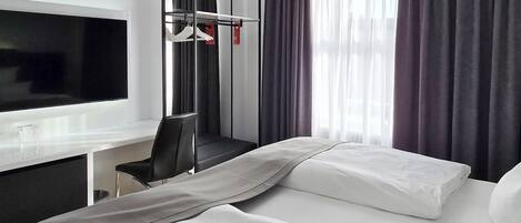 A hotel room with a bed, a desk with a TV, a chair, and a wardrobe.
