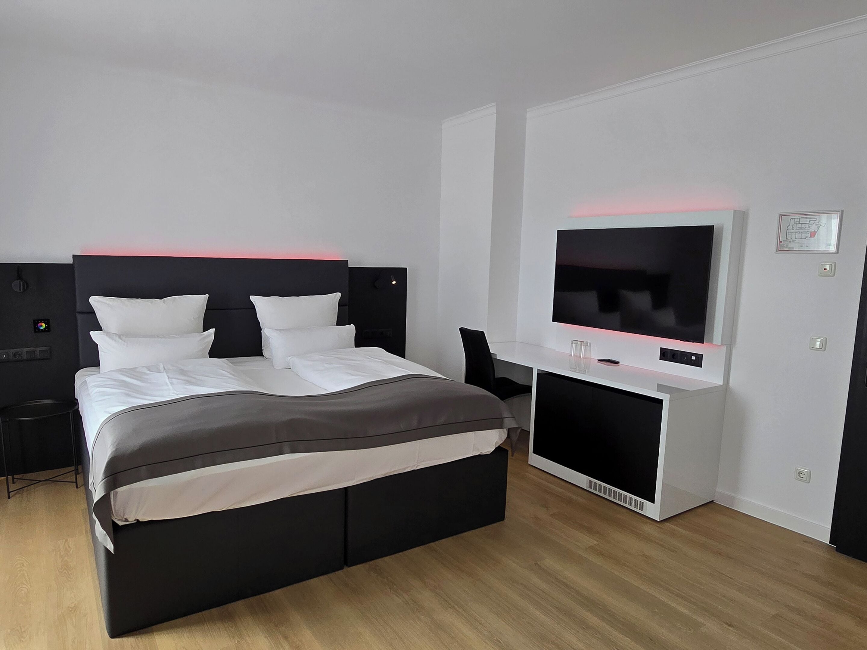Ein modernes Hotelzimmer mit einem großen Bett, einem flachbildfernseher an einer weißen Kommode und einem kleinen Schreibtisch mit Stuhl.