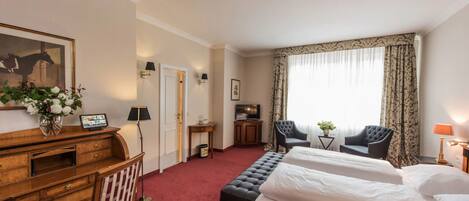A hotel room with two beds, a desk with a chair, a television, and a large window with curtains.