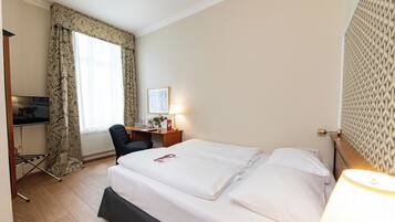 Habitación de hotel con cama, escritorio, silla, lámpara y ventana con cortinas.