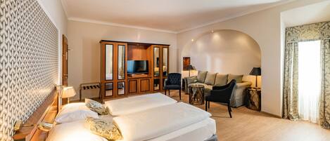 Une chambre d’hôtel avec un grand lit, une télévision, un coin salon avec un canapé et des fauteuils, et un mur décoré de motifs.