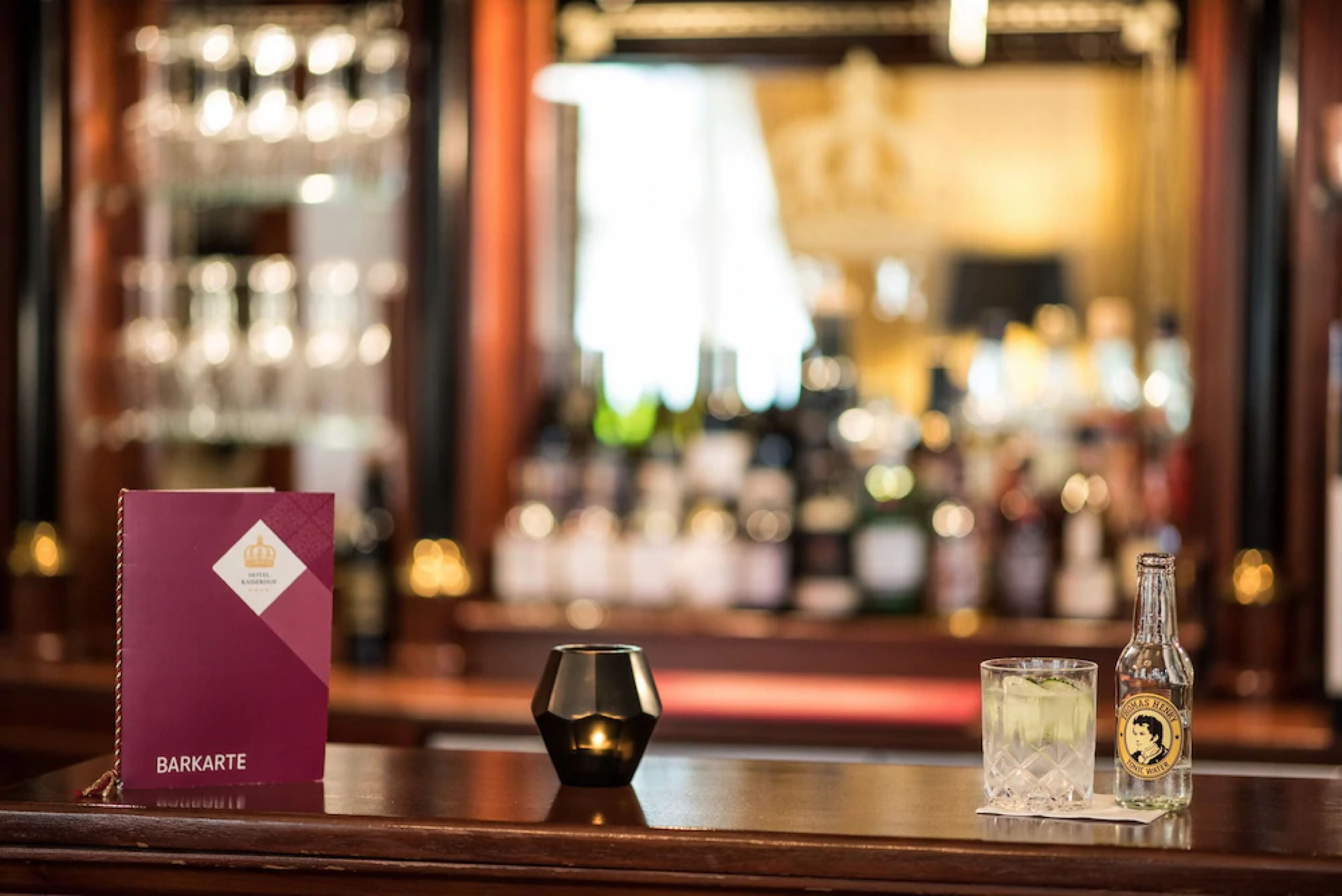 A bar area with a menu, a bottle of liquor, and a glass on a wooden counter.