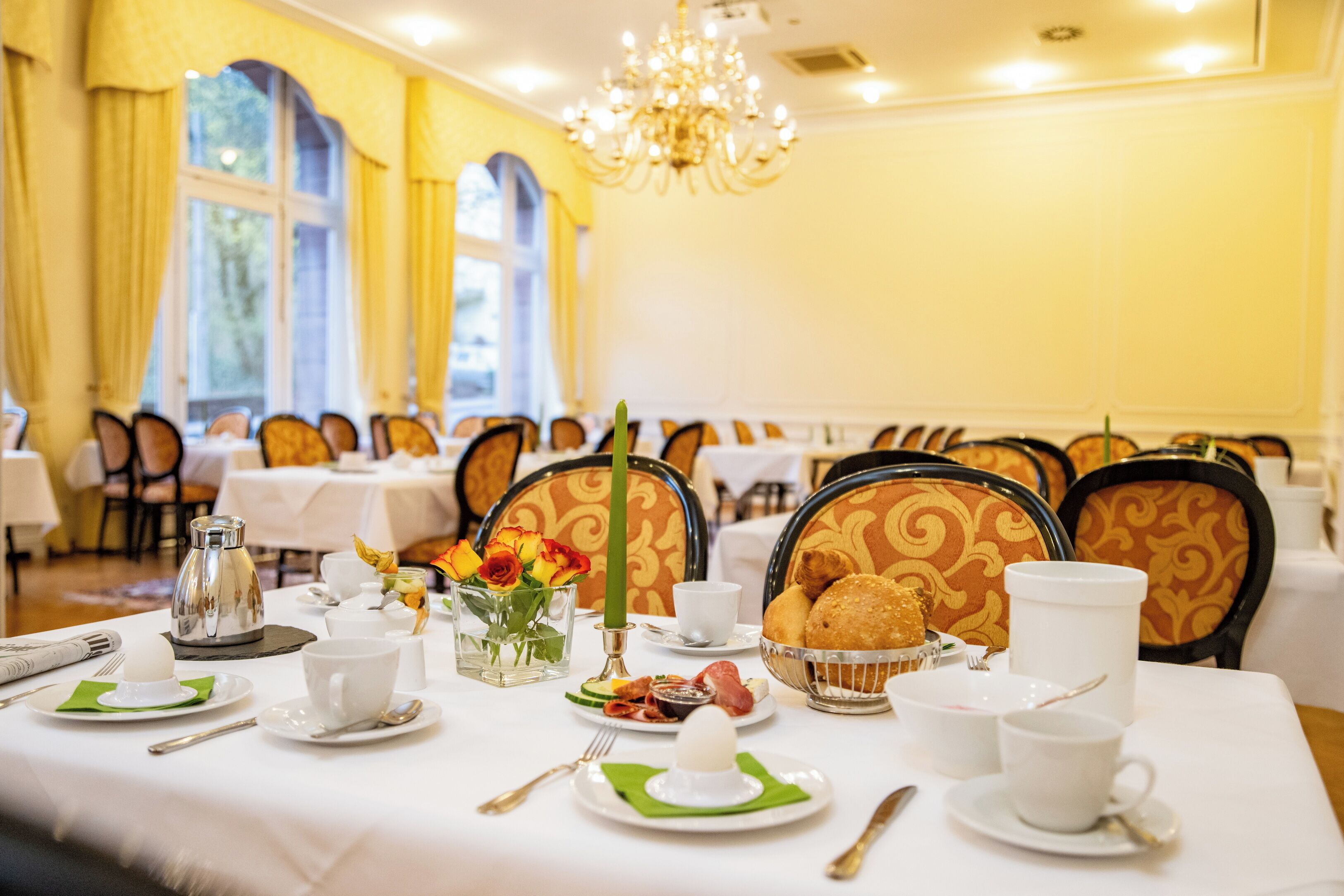 A dining table set with breakfast items, including eggs, pastries, and coffee, in a room with yellow walls and chandeliers.