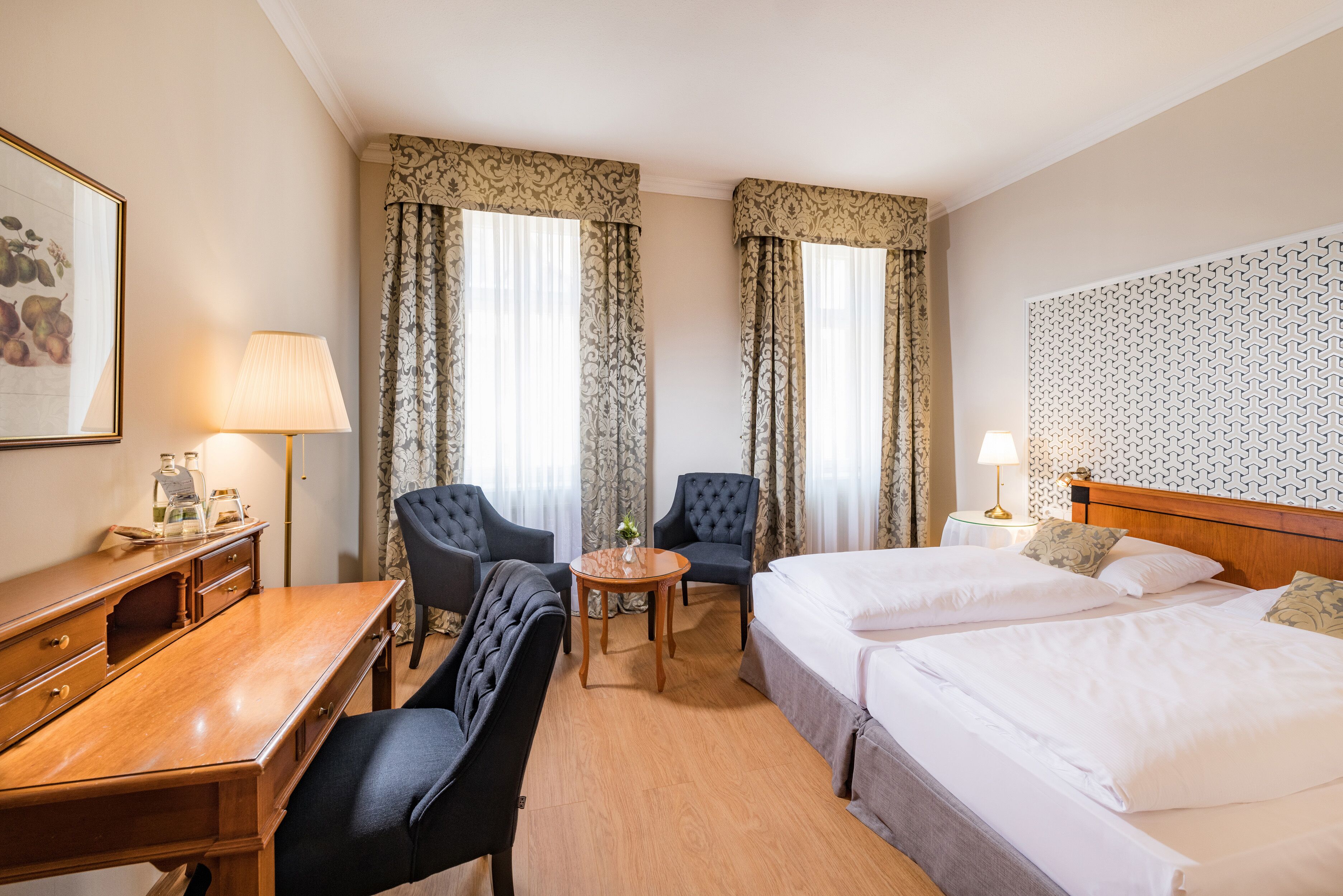 Una habitación de hotel con dos camas, un escritorio, dos sillones, una mesita y una lámpara.