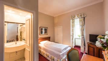 Ein Hotelzimmer mit Bett, Schreibtisch mit Fernseher, Badezimmer mit Waschbecken und Spiegel sowie einem Fenster mit Vorhängen.