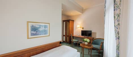 A hotel room with a bed, a desk with a chair, a television, and a framed picture on the wall.