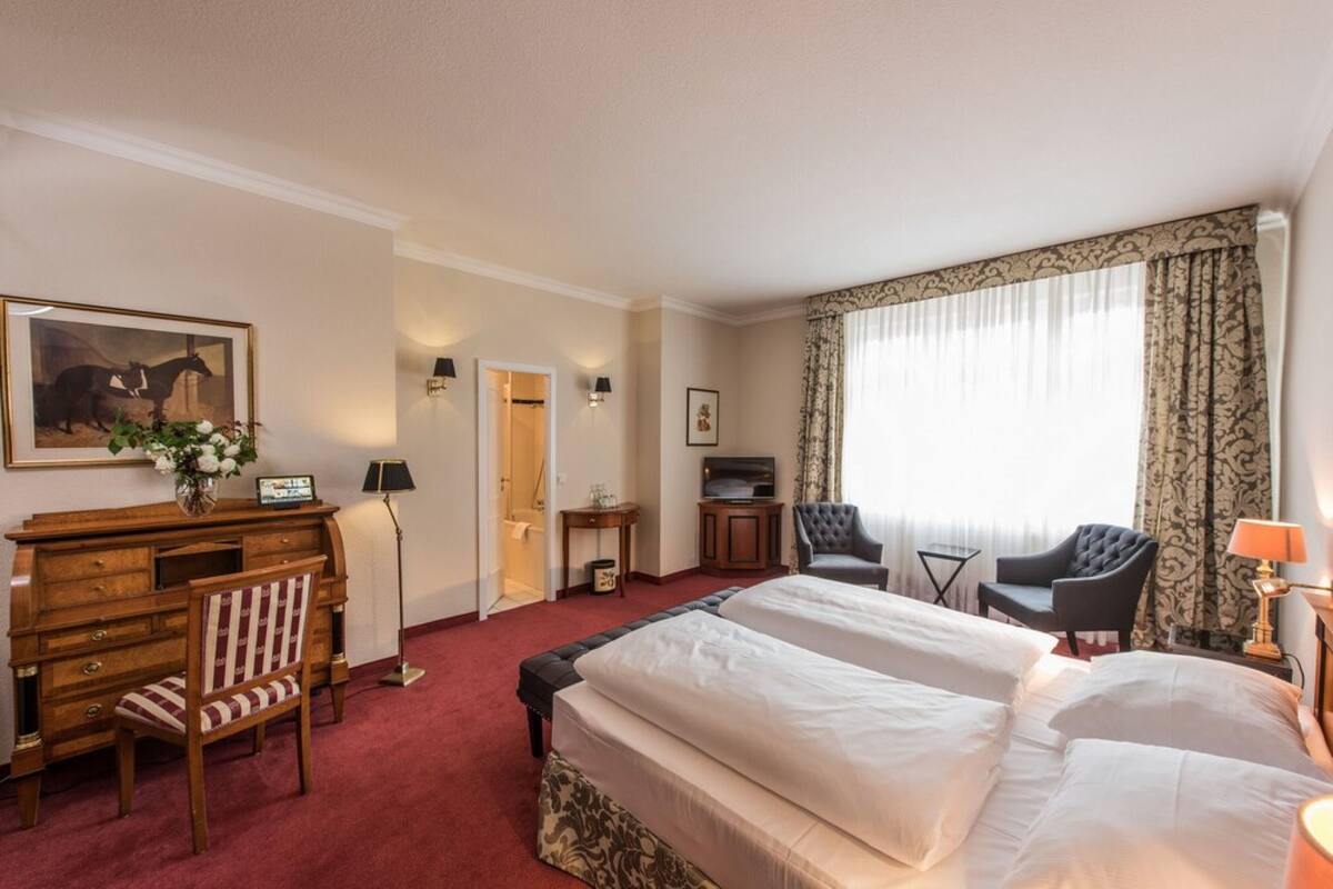 Hotellihuone, jossa on kaksi sänkyä, työpöytä tuolilla, televisio ja ikkuna, jossa on verhot.