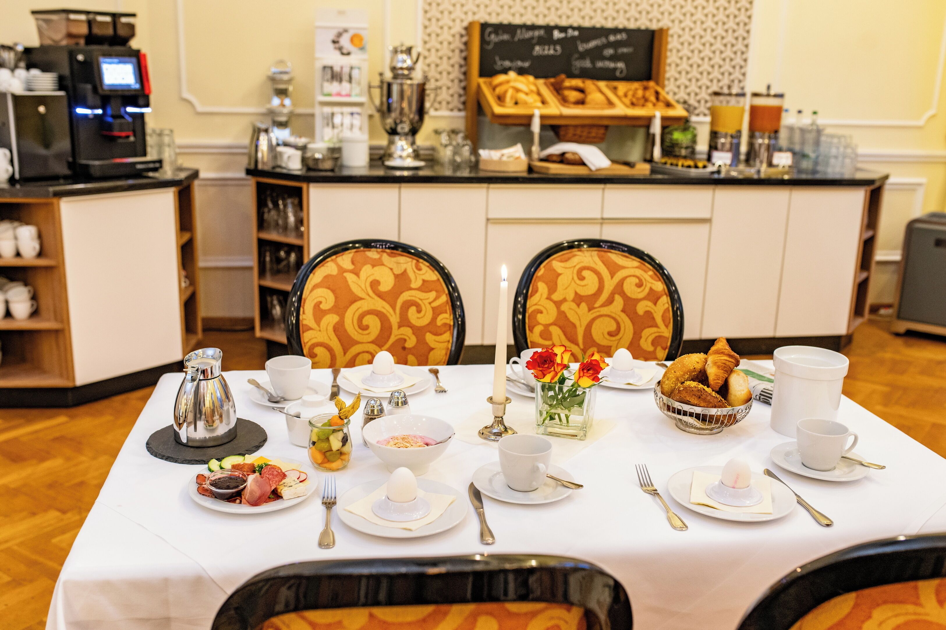 A breakfast setting with a coffee machine, a bowl of fruit, and a variety of pastries on a table.