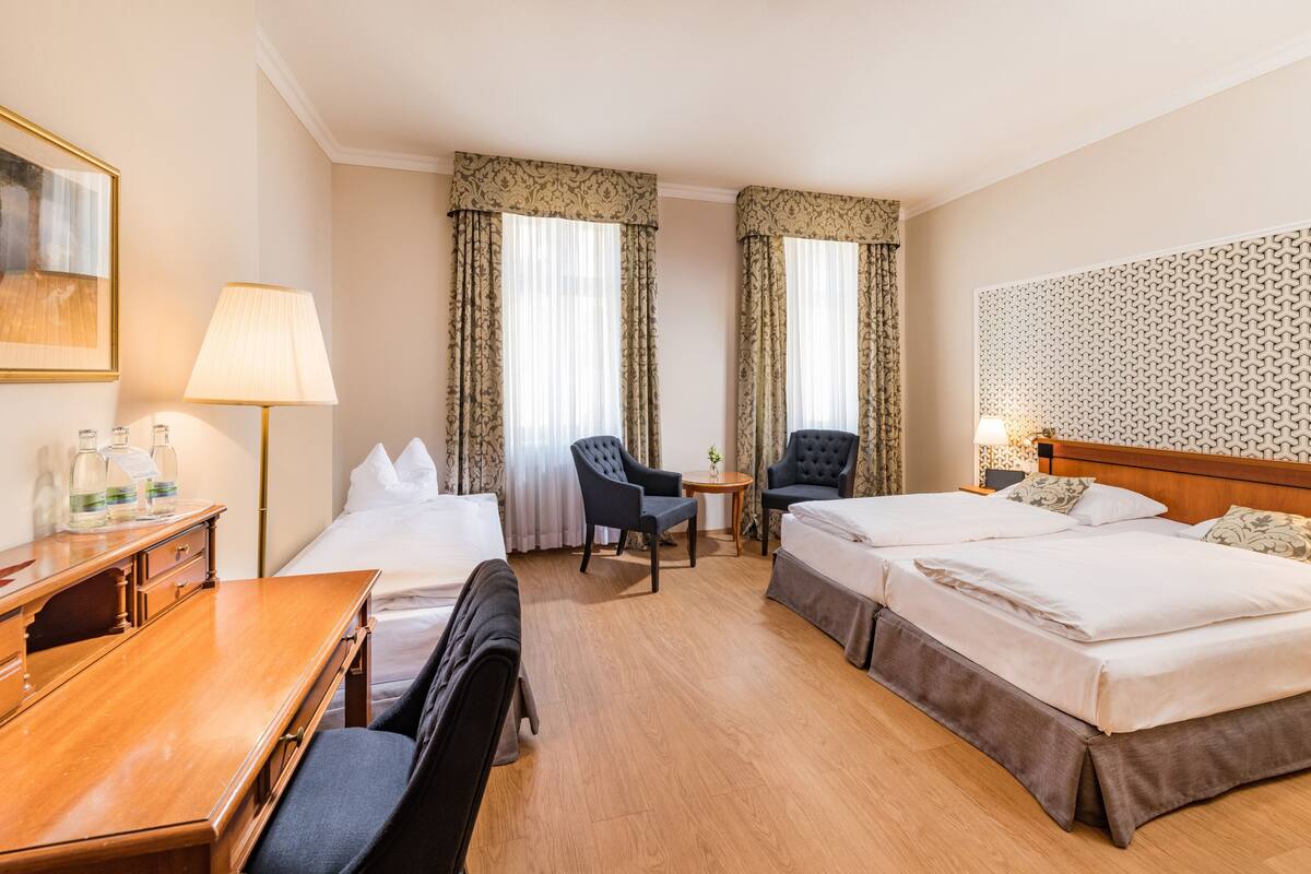 Hotellihuone, jossa on kaksi sänkyä, työpöytä, tuoli, pieni pöytä ja lamppu.