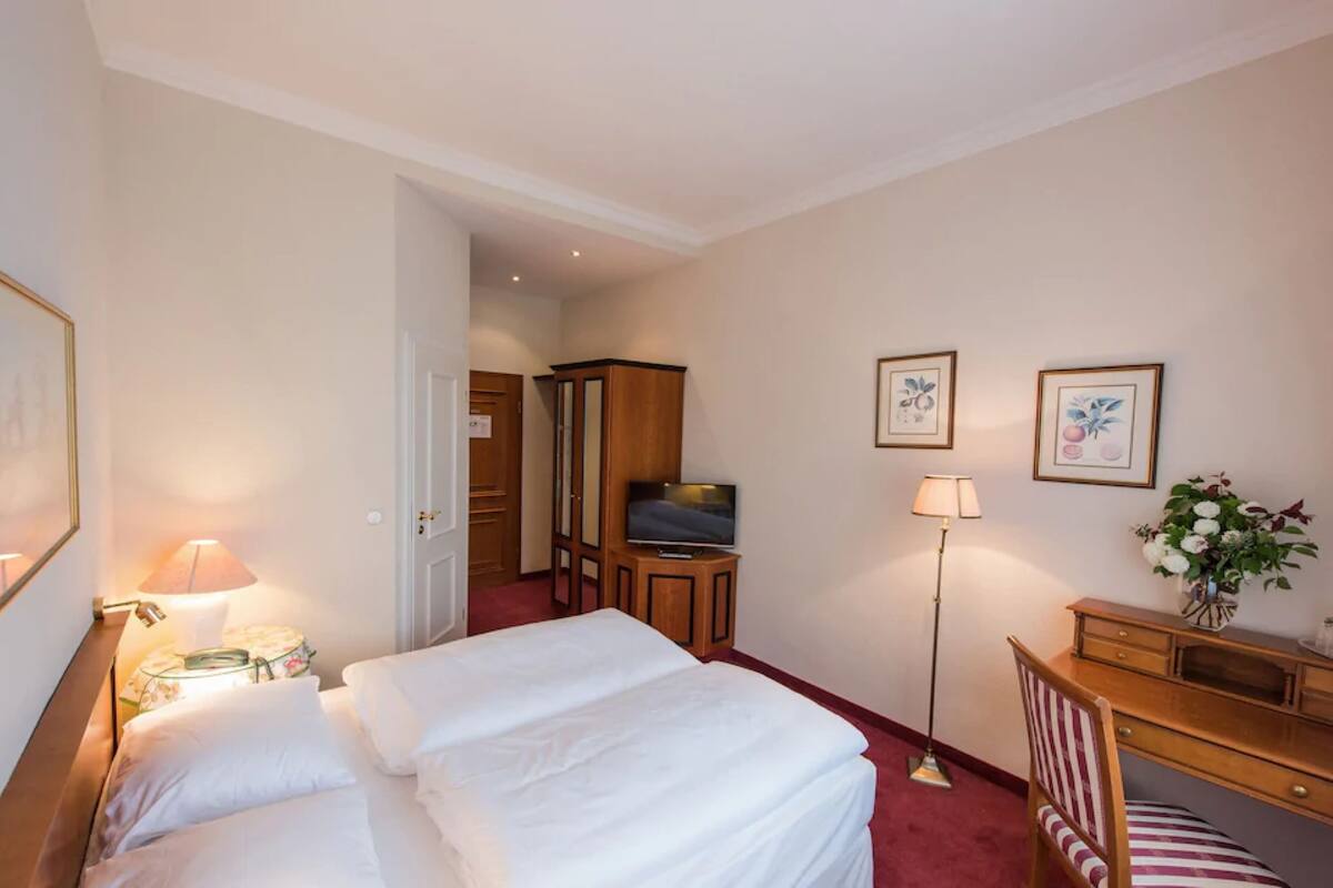 Hotellihuone, jossa on kaksi sänkyä, televisio, työpöytä ja kaappi.
