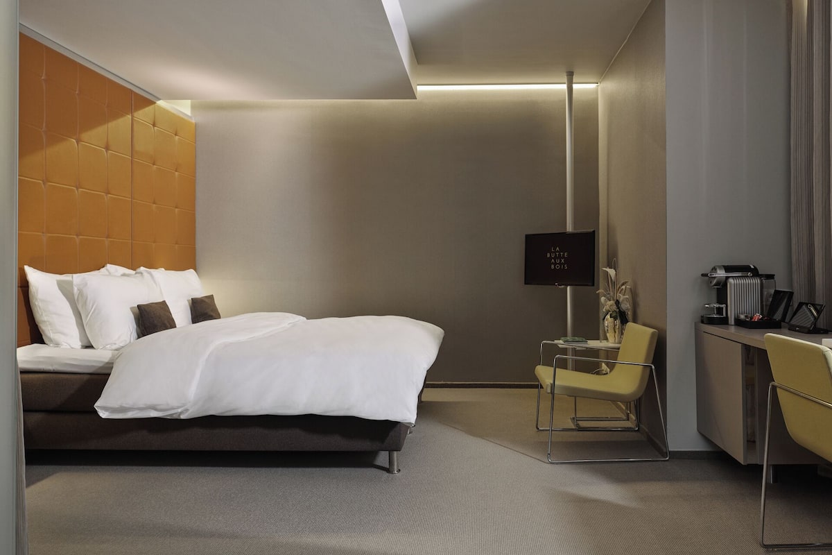 Una habitación de hotel moderna con cama, mesita de noche, silla y televisor de pantalla plana.