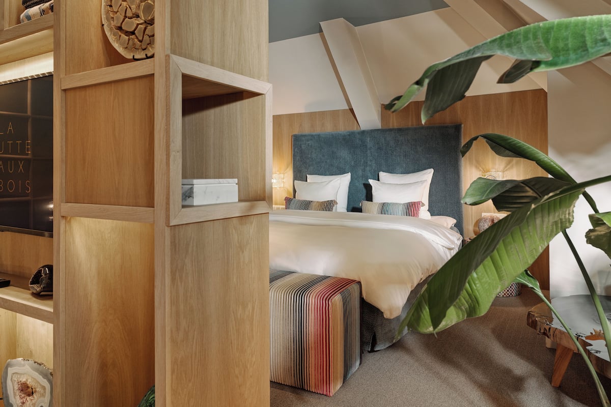 Un dormitorio con cama, mesita de noche, estante de madera y una planta grande.