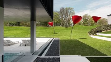 Un espacio exterior moderno con piscina, sillones de descanso y esculturas cónicas rojas.