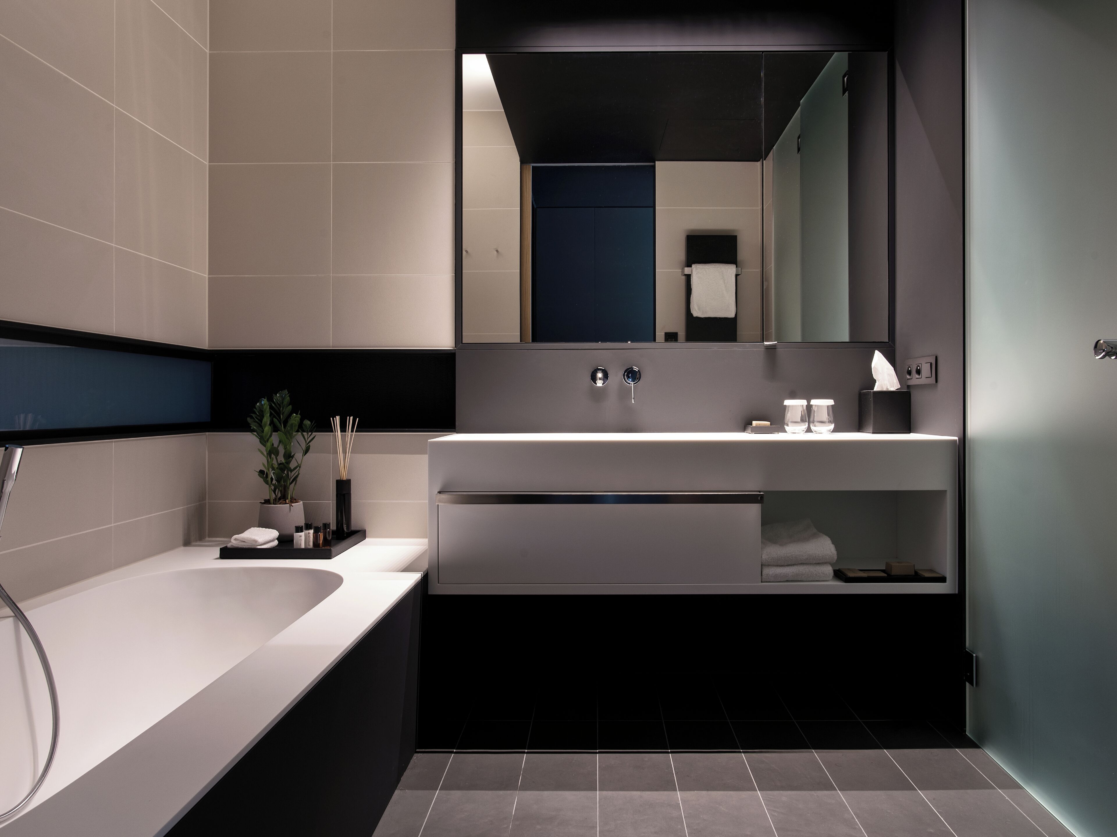 A modern bathroom with a bathtub, a sink with a mirror, and a shelf with toiletries.