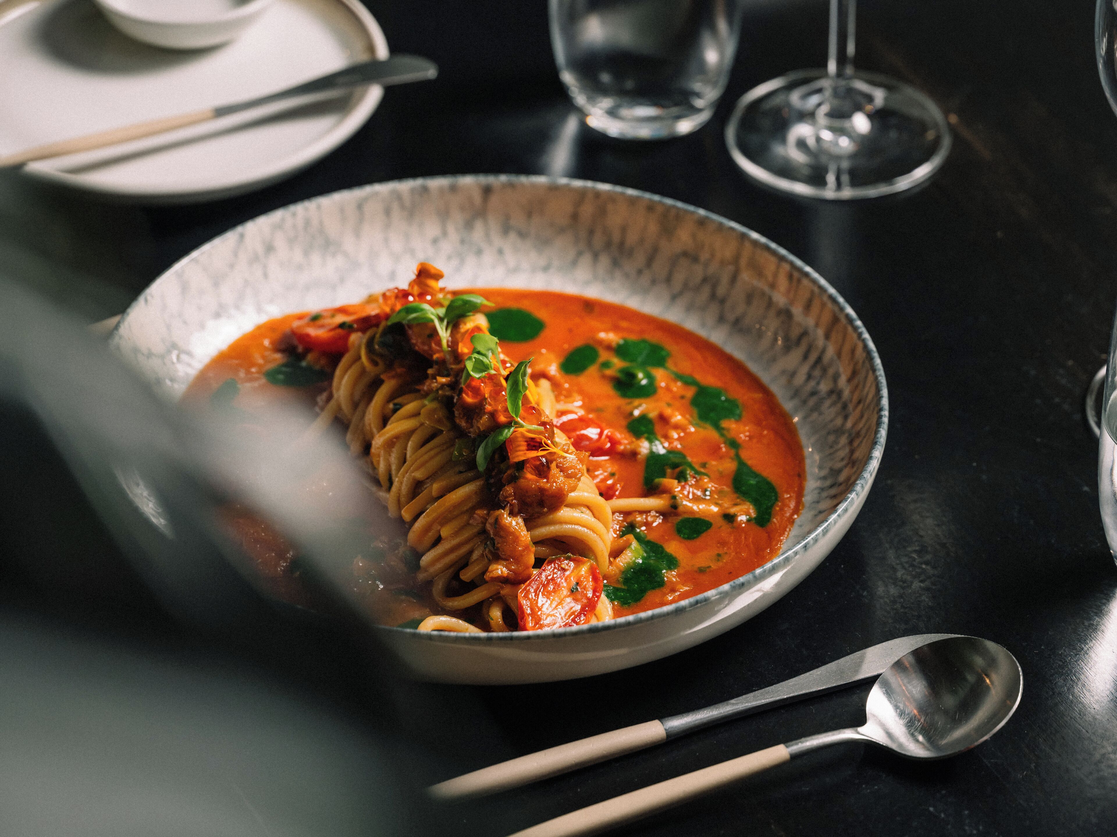 Un plat de pâtes nappées d’une sauce à base de tomates, garni d’herbes, posé sur une table sombre.