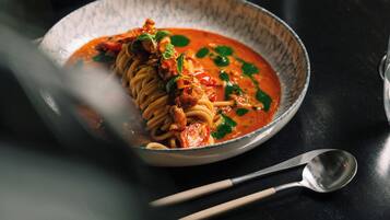 Un plat de pâtes nappées d’une sauce à base de tomates, garni d’herbes, posé sur une table sombre.