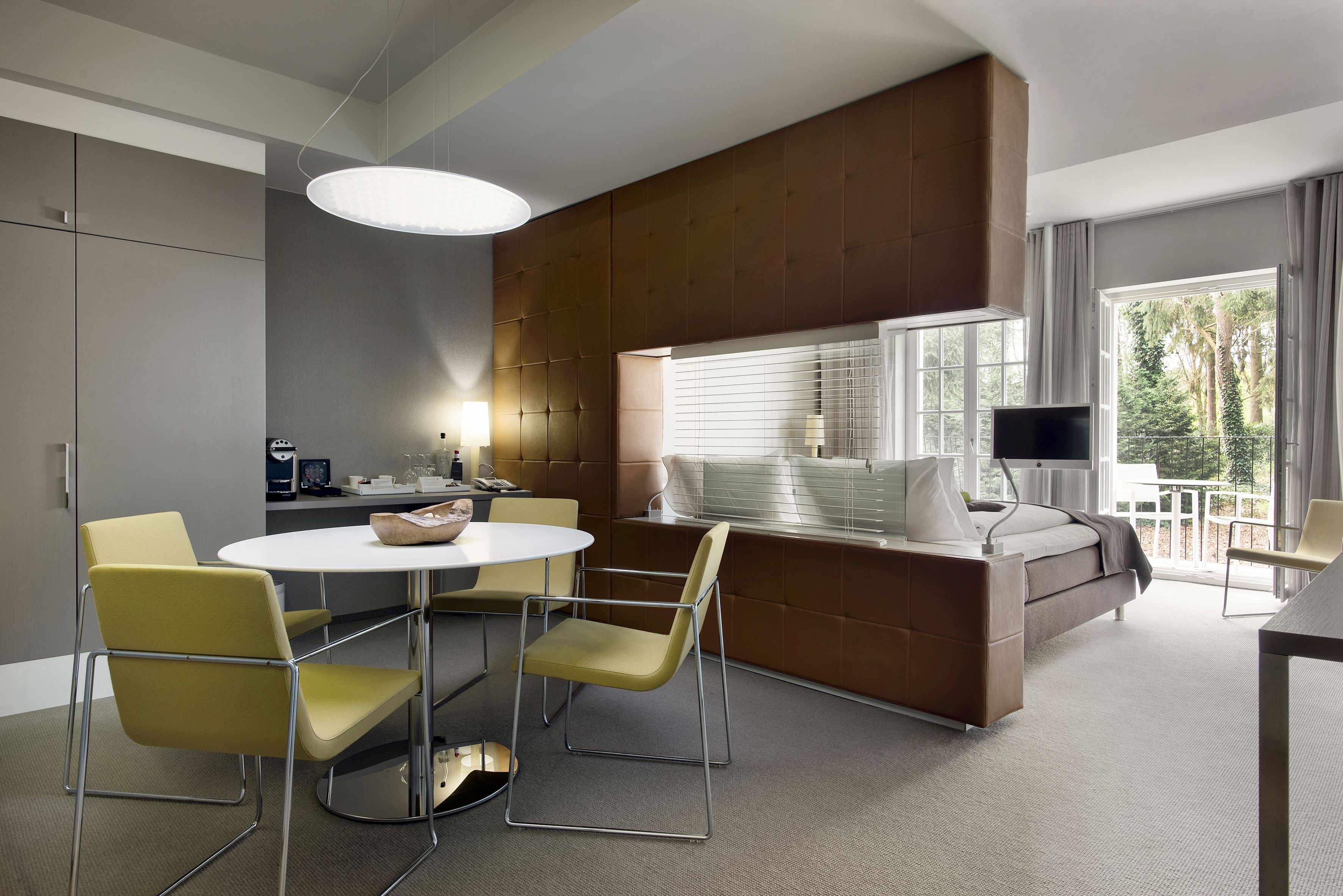 A modern hotel room with a dining area, a sofa bed, and a TV.