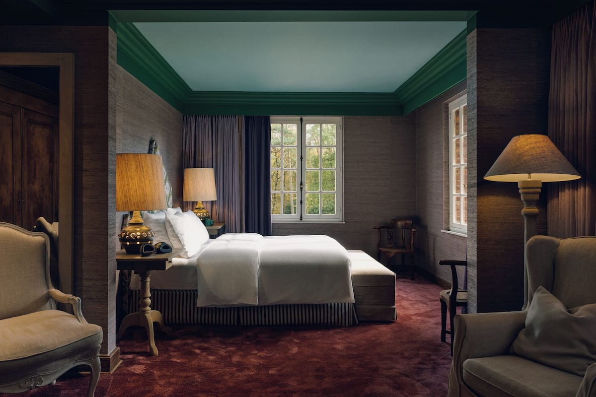 Un dormitorio con una cama grande, dos mesitas de noche con lámparas, una silla y una ventana con cortinas.