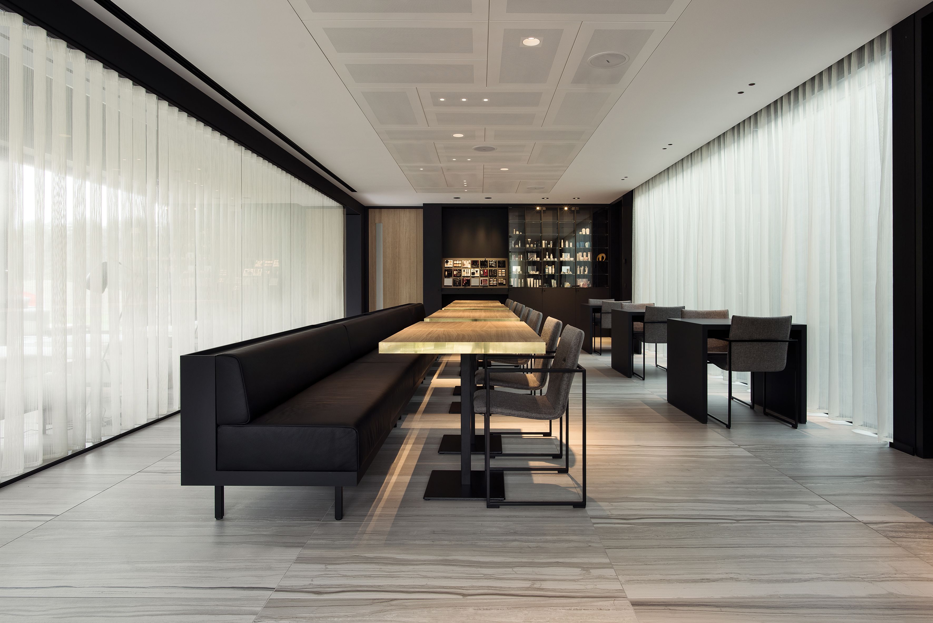 Un comedor moderno con una larga mesa de madera, bancos tapizados de color negro y una vitrina de vidrio al fondo.