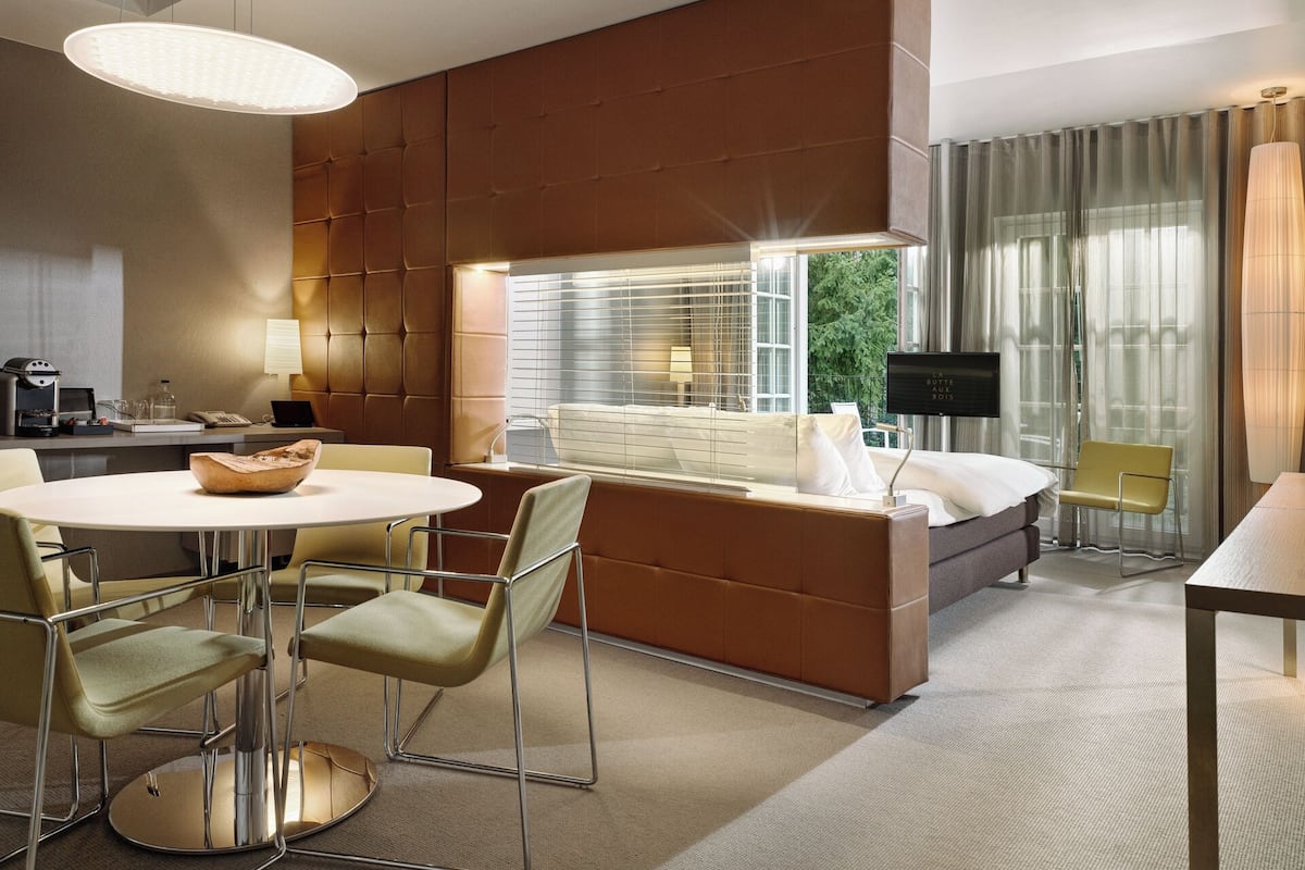 Una habitación de hotel moderna con sofá cama, zona de comedor con mesa redonda y sillas, cafetera y televisión.