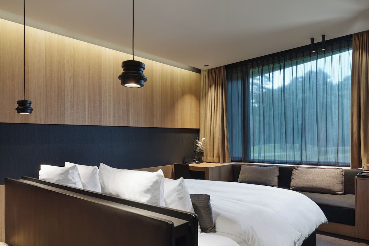Una habitación de hotel moderna con una cama grande, un escritorio y vistas al exterior a través de cortinas translúcidas.