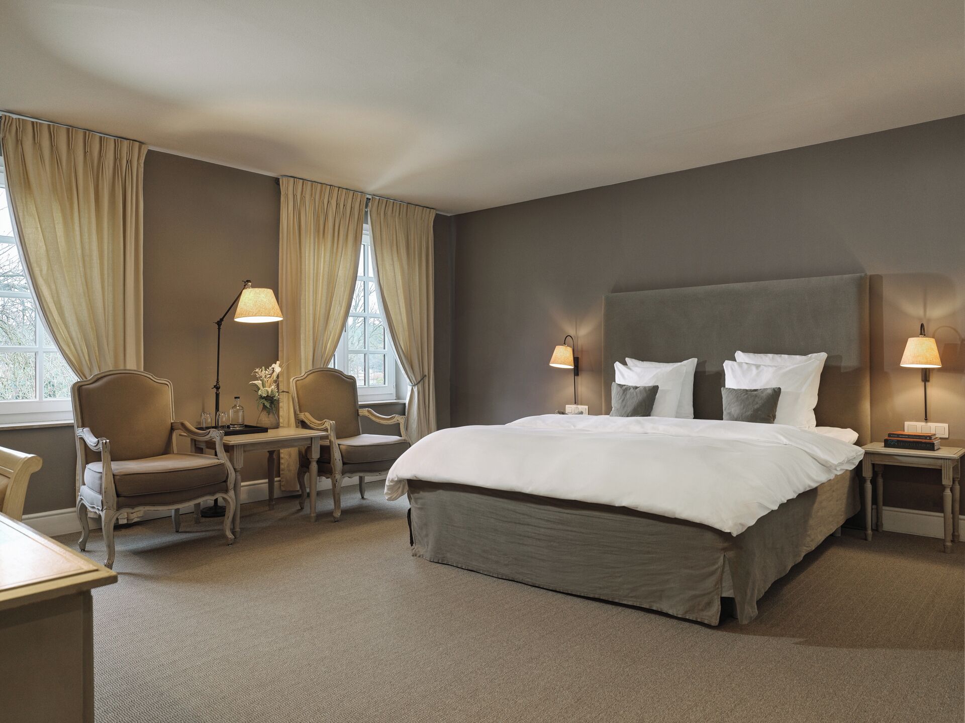 A hotel room with a large bed, two bedside tables with lamps, a chair, and a desk with a lamp.