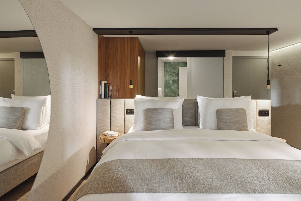Una habitación de hotel moderna con una cama grande, un panel de pared de madera y una mesita auxiliar con libros.