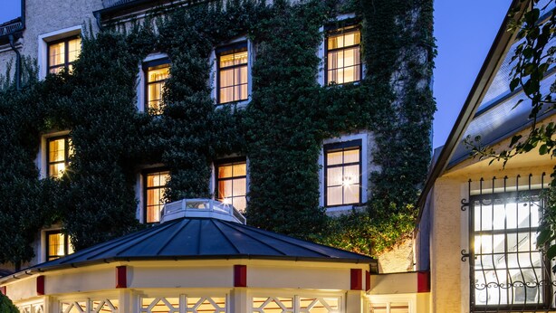 A building with ivy-covered walls, multiple windows, and a well-lit entrance.