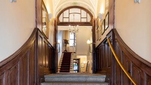 A grand staircase with ornate ceiling and wall decorations, leading to a well-lit interior space.