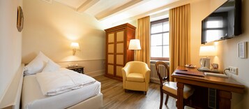 Una habitación de hotel con cama, escritorio, silla, televisor y ventana con cortinas.