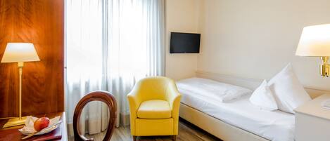 A hotel room with a wooden desk, a yellow armchair, a bed, and a flat-screen TV on the wall.