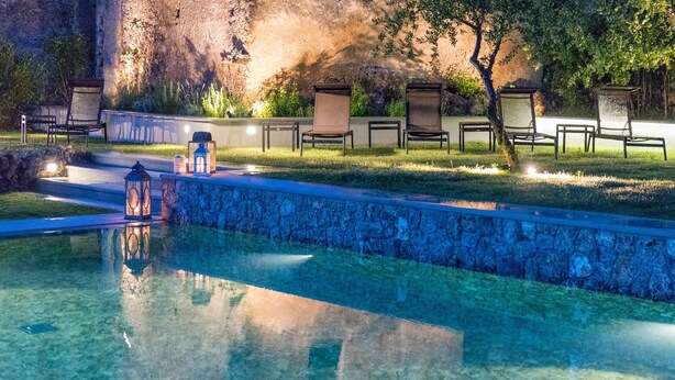 A swimming pool with clear water, surrounded by stone walls and a grassy area with outdoor seating. - Villa Cheta Hotel & Restaurant (Maratea)