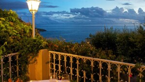 A balcony with a table set for two, overlooking a coastal view with a lamp post and lush greenery. - Villa Cheta Hotel & Restaurant (Maratea)
