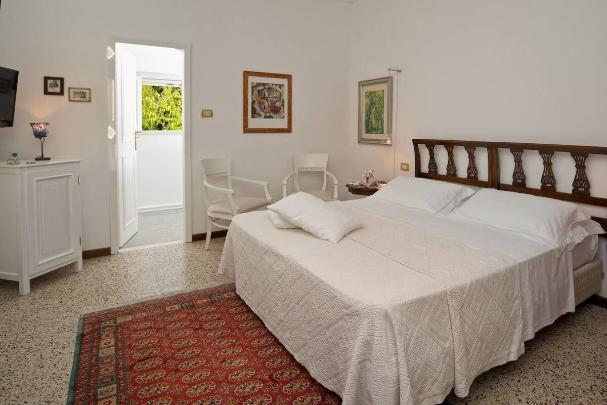 Une chambre avec un grand lit, une chaise, un bureau et une porte donnant sur un balcon.