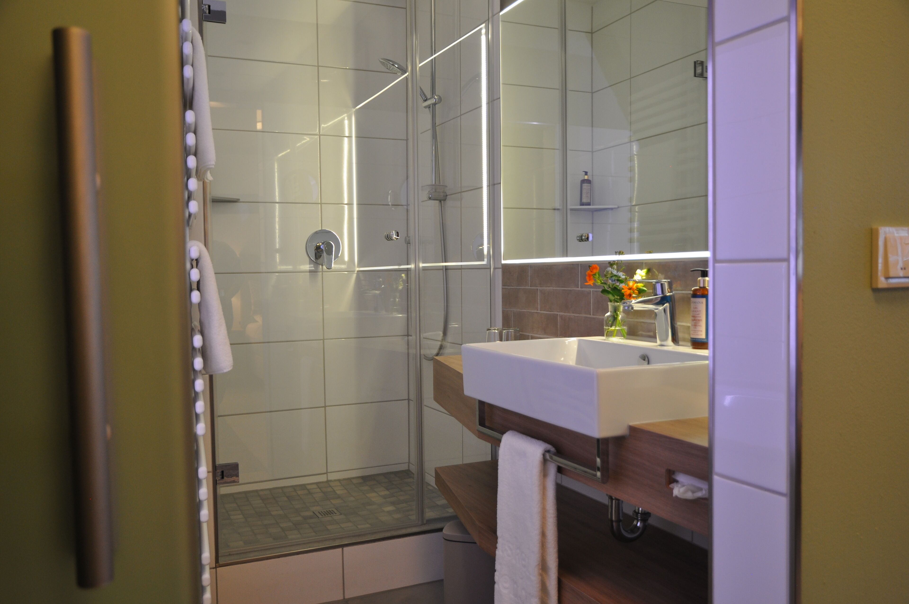 A modern bathroom with a glass-enclosed shower, a sink with a mirror, and a towel rack.