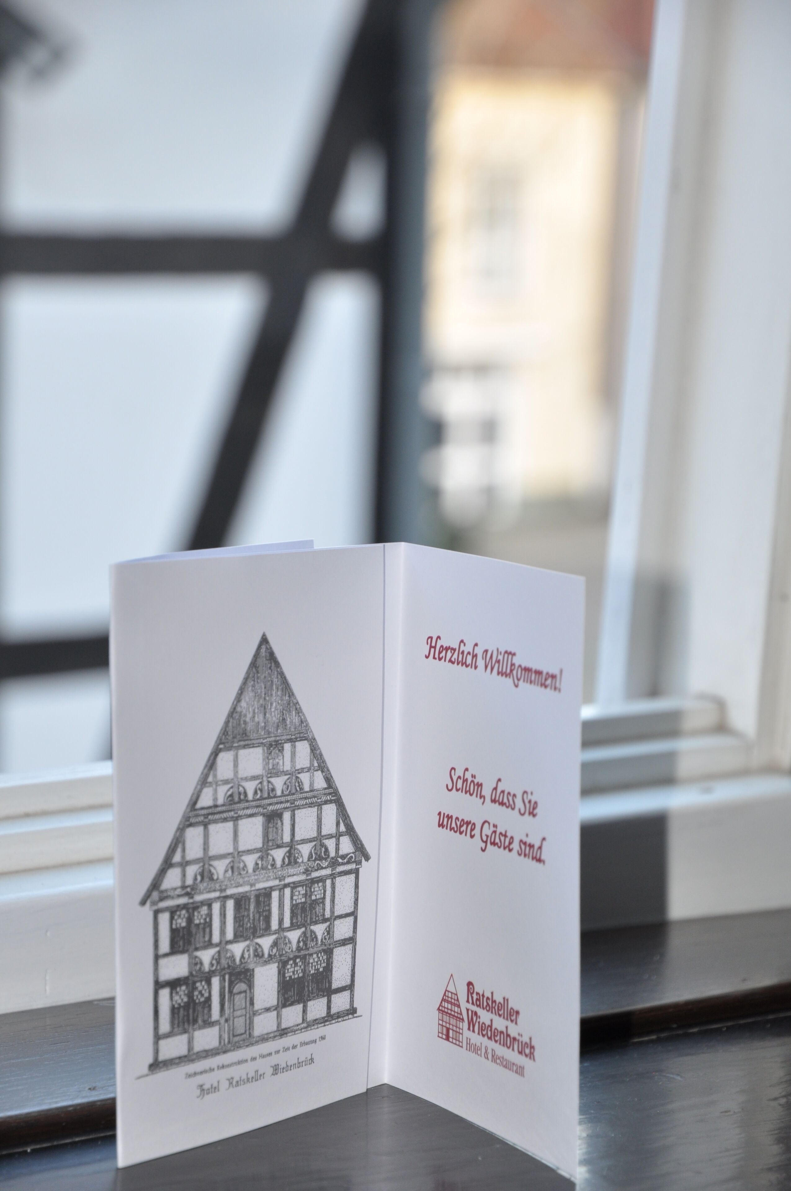 A brochure with a house illustration and text in German, placed on a windowsill.